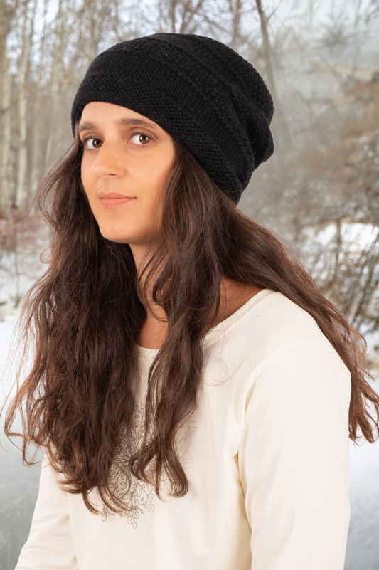 Woman wearing a black knit beanie and white sweater outdoors with trees in the background