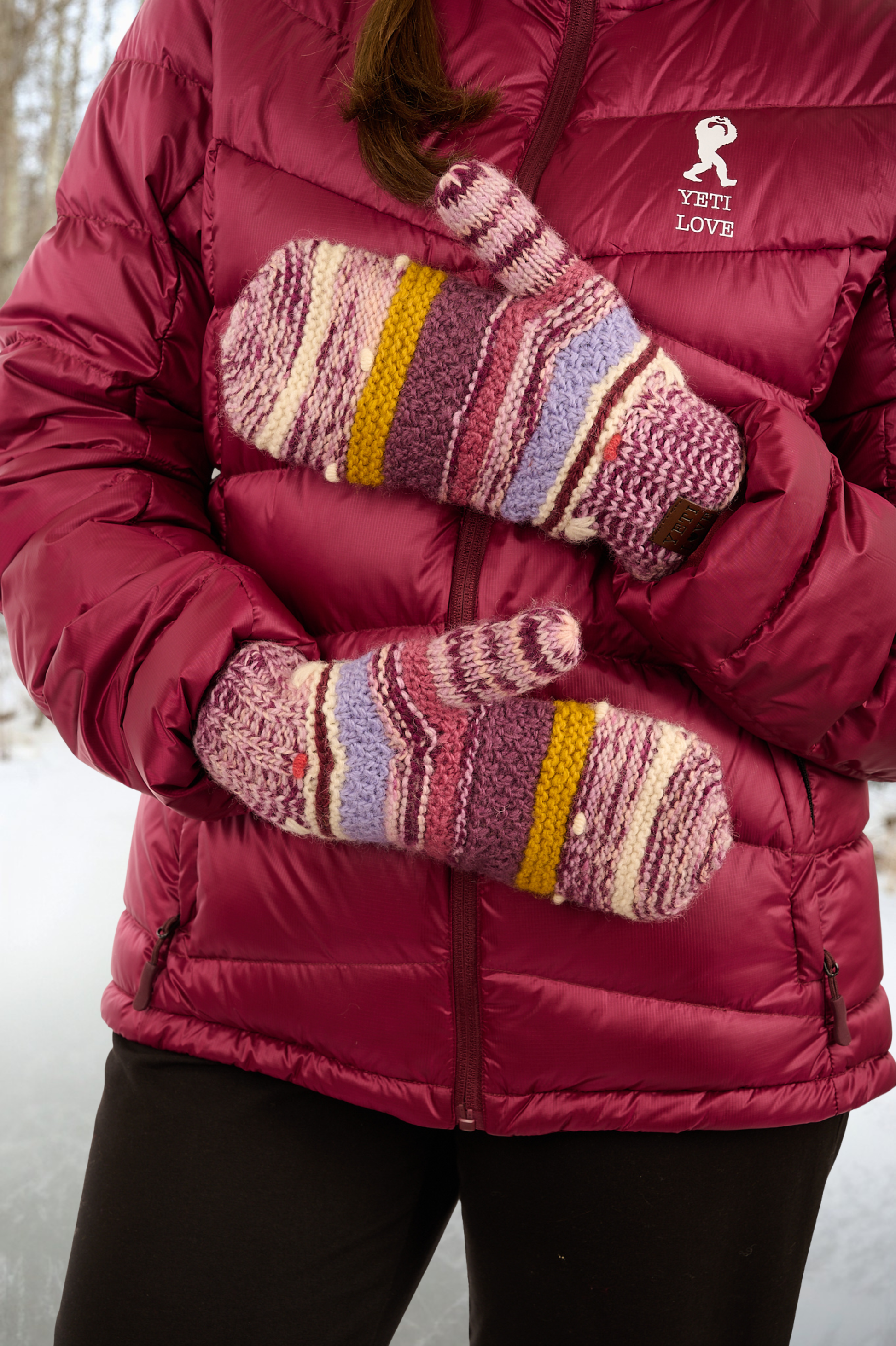 Person wearing a red puffer jacket and colorful mittens with a snowy background